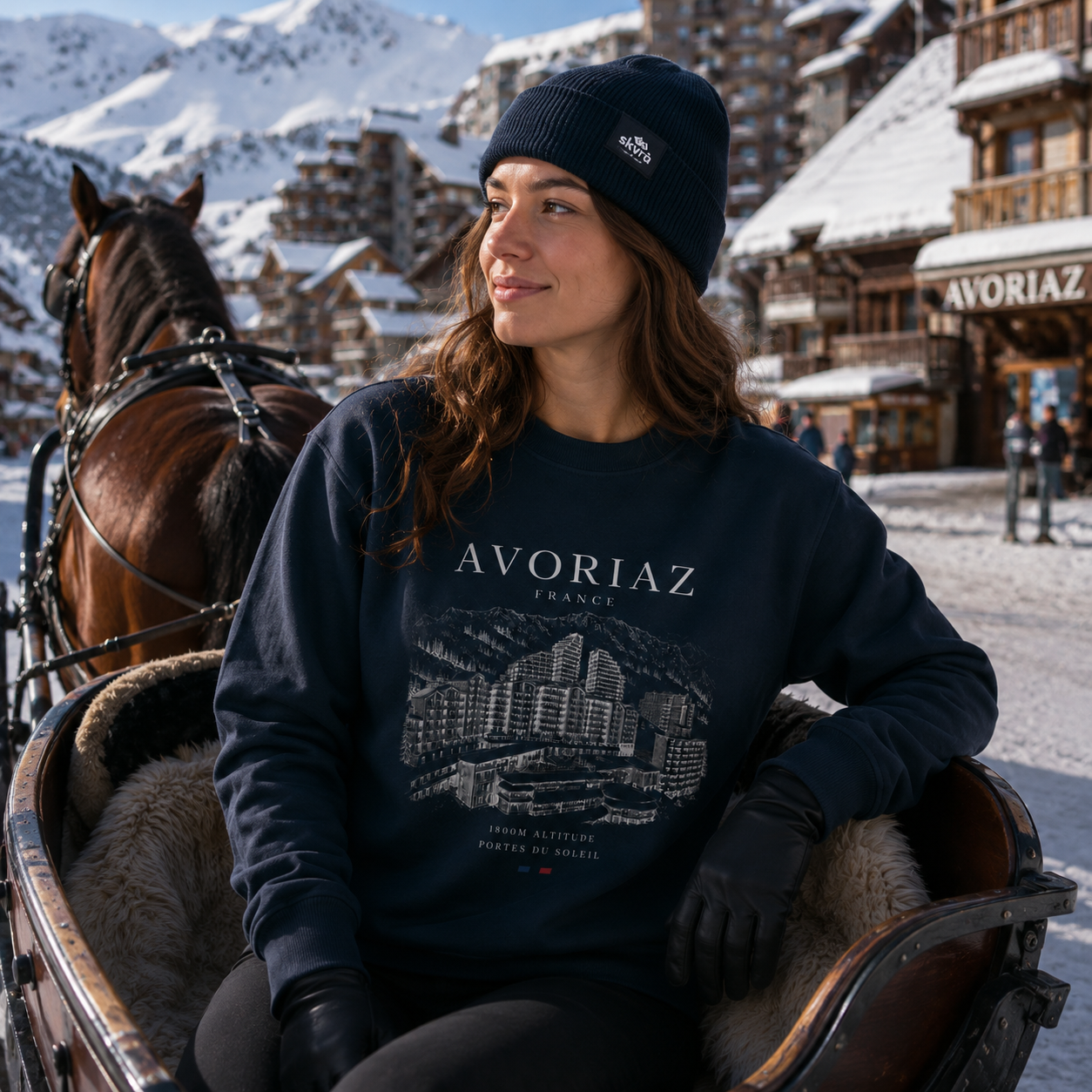Woman in a 'Avoriaz France' sweatshirt sitting in a horse-drawn carriage with a snowy mountain village background.