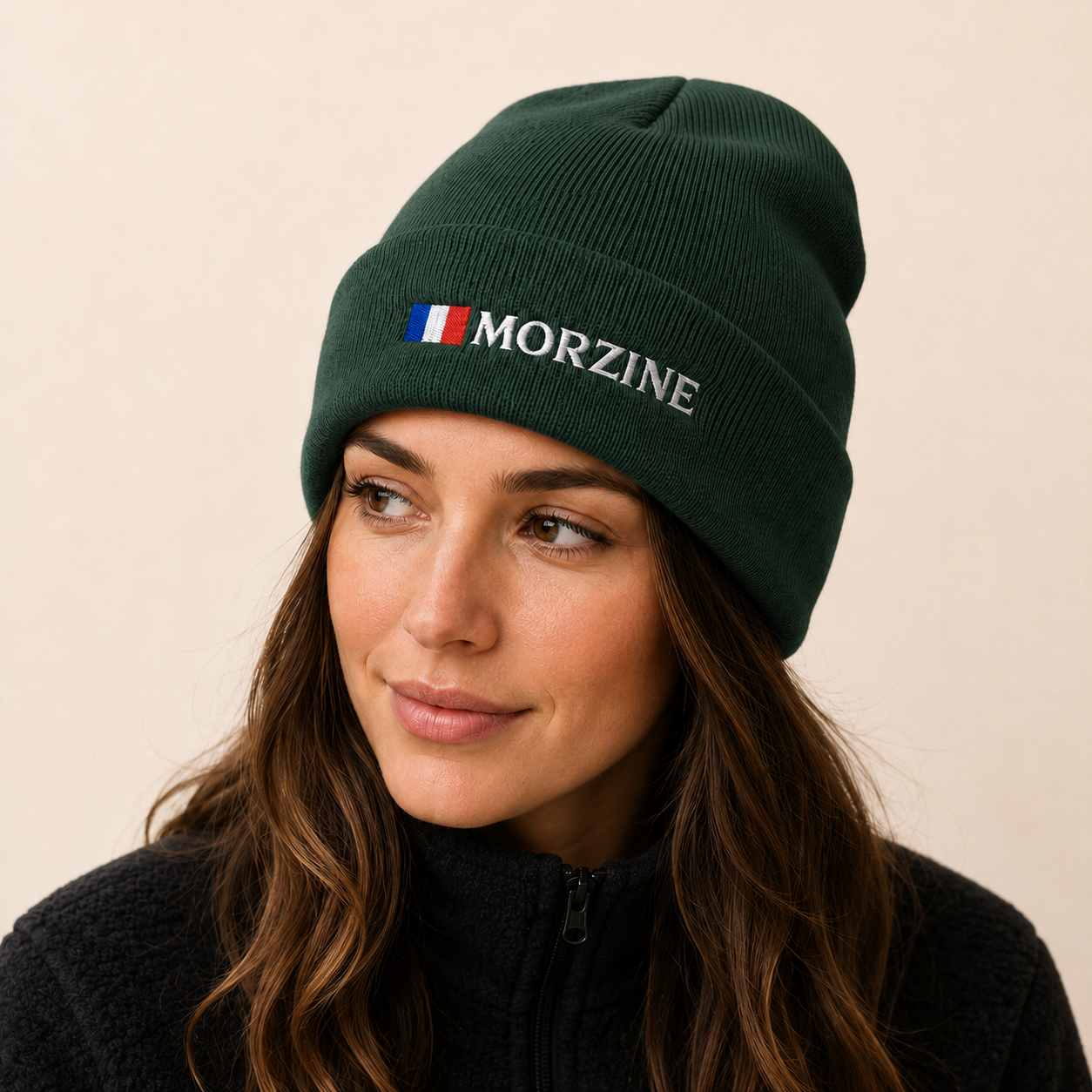 A woman wearing a dark green ribbed knit beanie with a small French flag embroidered on the front next to the white embroidered text 'MORZINE'.