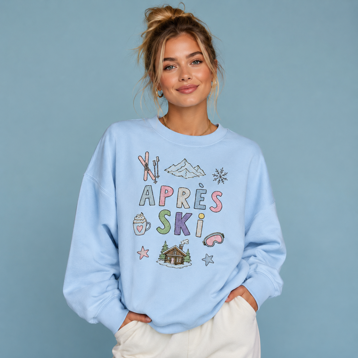 Woman wearing a light blue sweatshirt with 'Apres Ski' graphics on a solid background