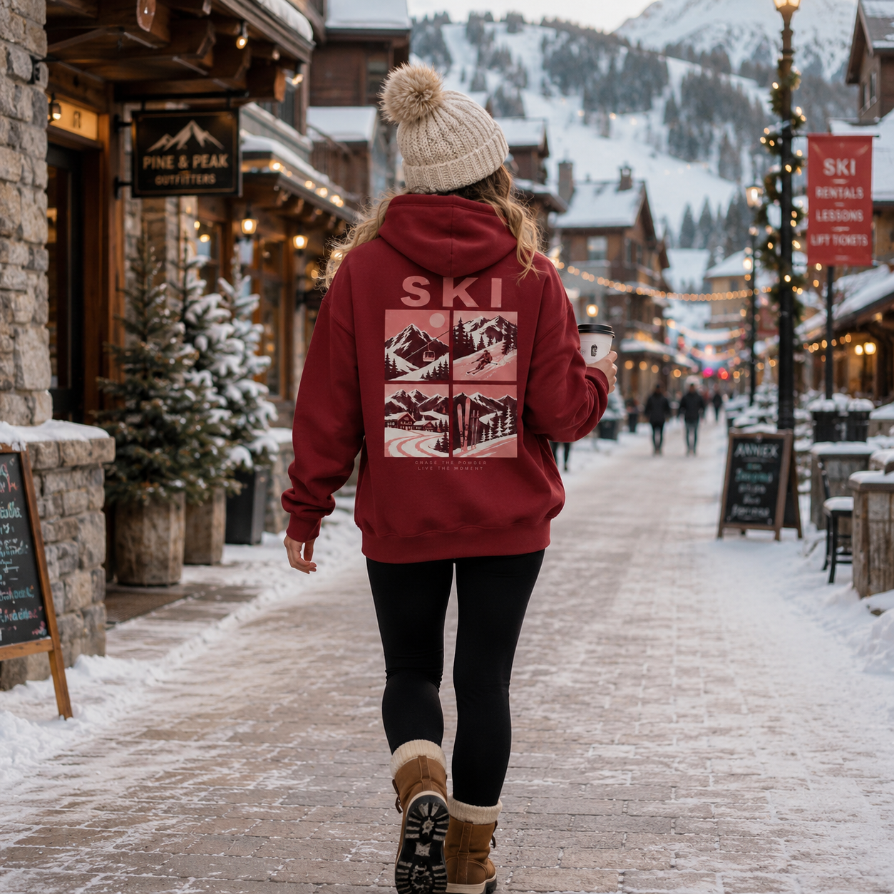 Person wearing a red hoodie with 'Ski' and mountain design, walking through a snowy village street.